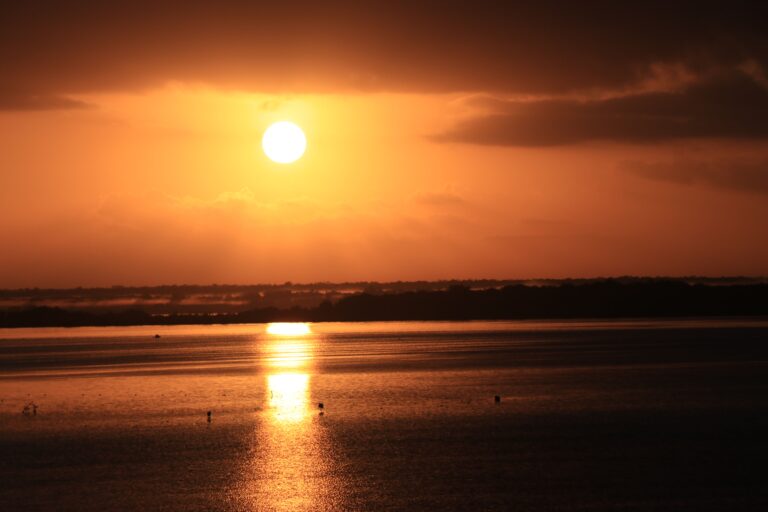 A mesmerizing sunset over a tranquil lake with vibrant orange hues reflecting on the water's surface.