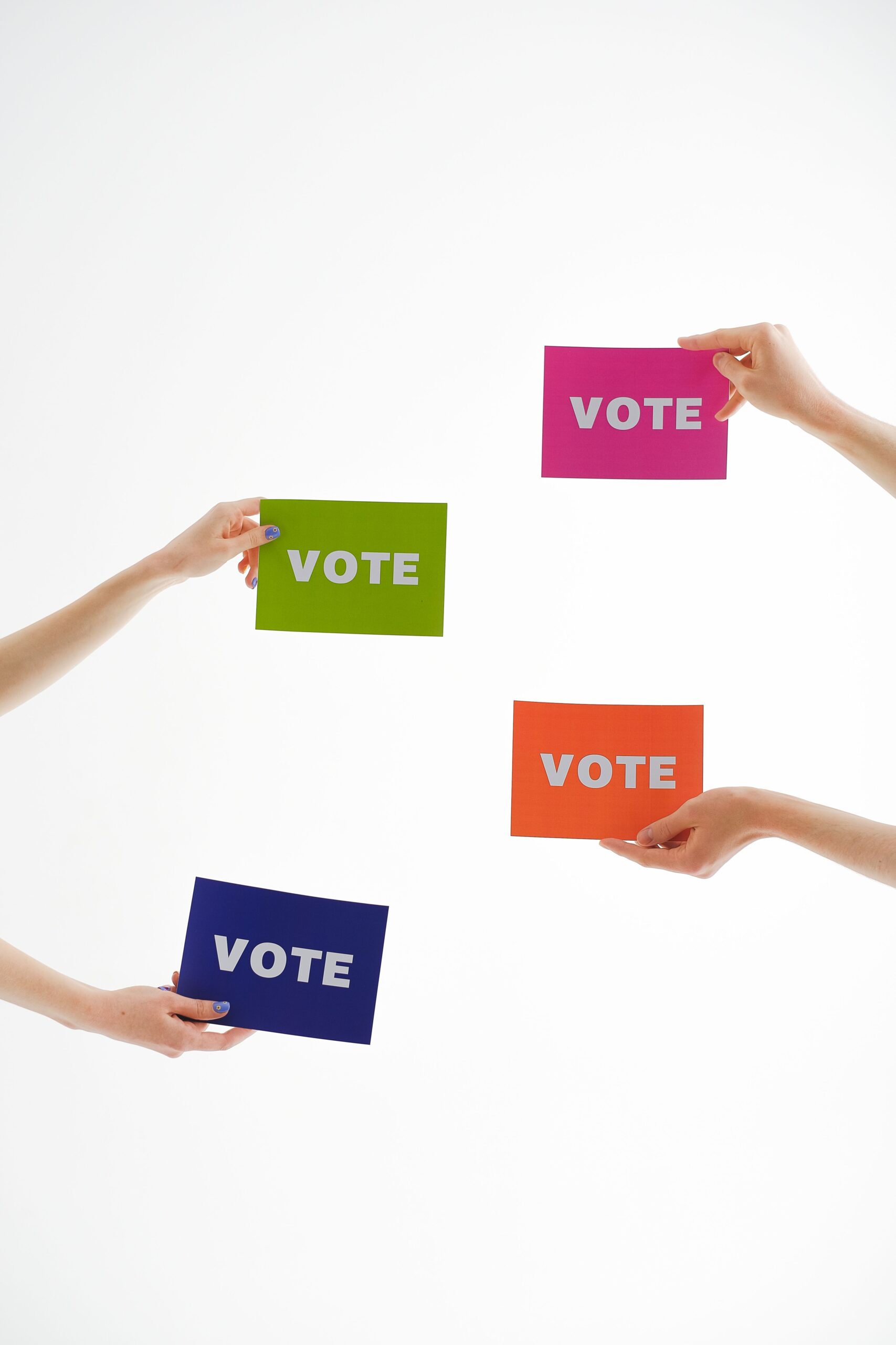 Four hands holding colorful 'vote' cards, emphasizing democracy and participation.